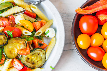 Plate with penne pasta with tomatoes, zucchini, mozzarella and basil and a plate with cherry tomatoes - top view, close-up.