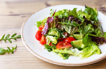 Bowl of salad with vegetables on wooden table.