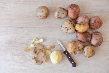 raw potatoes in the process of cleaning lies on a wooden table next to a small knife. cleaning, peel. clean potatoes