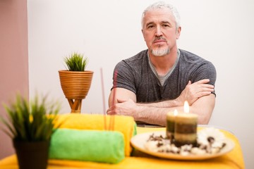 Adult gray-haired male masseur sitting at a workplace in a beauty salon