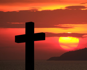Cross and crucifixion of Jesus Christ silhouette with fiery red dramatic sky and massive glowing large sun over an island during sunset. Religious symbolism, Mourning, memories, remembrance and commem