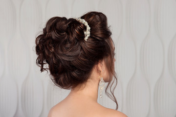 Naklejka premium Wedding female hairstyle medium beam on the head of a brunette girl close-up rear view on a light background.
