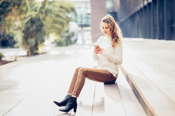 Schöne junge Frau sitzt in casual Kleidung draußen auf Stufen mit Handy in der Hand Nachricht...
