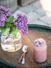 Glass of smoothie with blueberries and banana. Blossoming lilac flowers on wooden table..