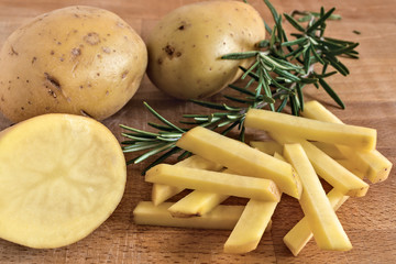 patate taglate a stick e rosmarino su tagliere di legno