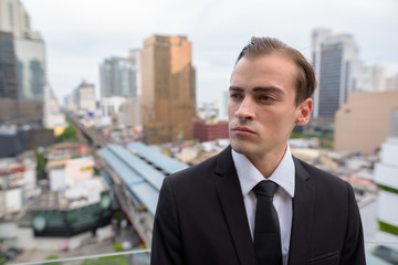 Fototapeta na wymiar Young businessman thinking outdoors in city with rooftop view