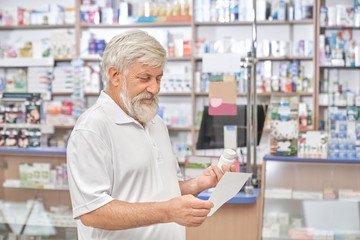 Naklejka na ściany i meble Pensioner looking at prescription in drugstore.