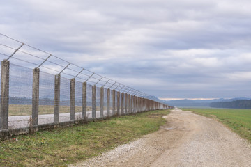 Fototapeta na wymiar Long country road stretching off past a lone tree to the distant horizon with fence on the right