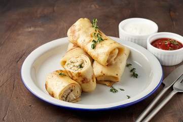 Savory crepe rolls with ground meat filling served with sour cream and tomato sauce