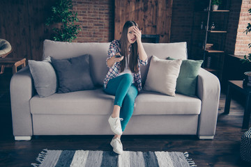 Fototapeta premium Full length size photo portrait of scared beautiful curious funky she her lady holding remote control in hand sitting on divan in light loft room