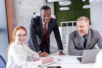 Ethnic business team African man with red-haired girl with gray-haired adult man working at the...