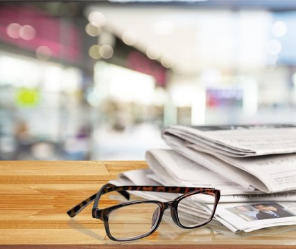 Newspapers with reading glasses on background