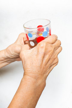 Senior woman's hand holding polka dot glass, drinking water on white background