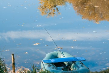fishing rod in a rubber boat, small lake, trees and sky reflection on still water surface, cold...