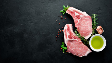 Raw steak on the bone. Meat with spices and herbs. On a black stone background. Top view. Free copy...