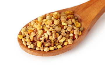 Bee pollen grains in wooden spoon isolated on white background