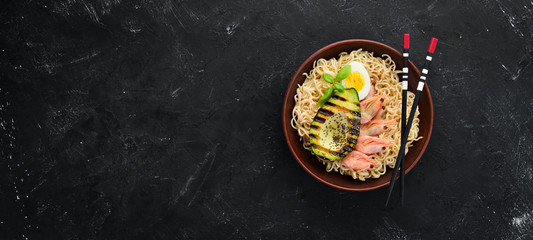 Asian food. Noodles with shrimps, avocados, eggs and chia seeds. On a black stone background. Top view. Free copy space.