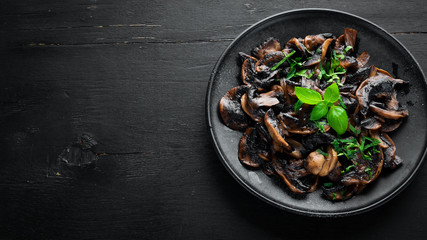Fried mushrooms with parsley on the plate. On a black background. Top view. Free space for your text.