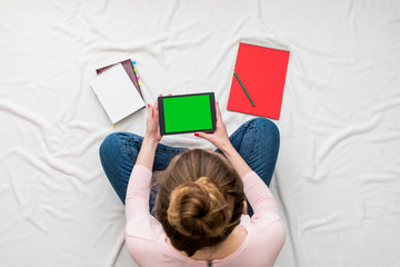 Woman holding a tablet, sitting on a white crumpled blanket, red notebook, women's feet. Women's hands. Background with copy space, for advertisement. Top view