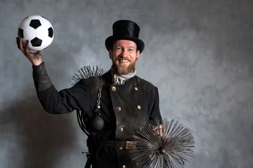 Fotobehang Kaminfeger in Arbeitskleidung und Kehrgeräten, hält lachend Ball in der Hand © Werner