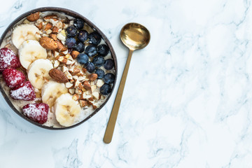 Healthy breakfast berry smoothie coconut bowl topped with blueberry,almond, banana, granola and raspberries. Top view. white marble background. Copy space.