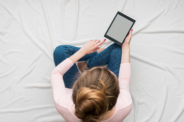 Woman using tablet, women's feet, sitting on a white crumpled blanket. Women's hands, close up. Background with copy space, for advertisement. Top view