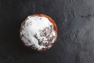 Homemade muffin with sugar powder on the dark, textured background, top view