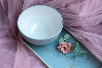 Empty ceramic bowl and tray with green branch on pink textile background.