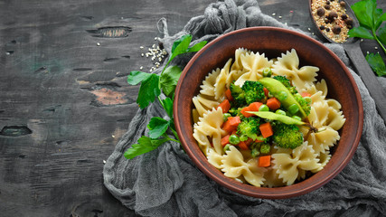 Farfalle pasta with vegetables on the plate. Top view. On a black background. Free copy space.