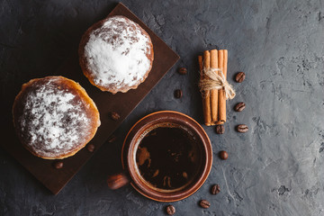 Cup with hot coffee, muffins and cinnamon sticks on the dark, textured background, top view