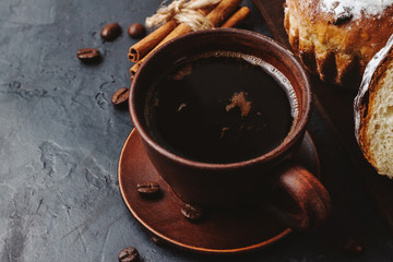 Cup with hot coffee, muffins and cinnamon sticks on the dark, textured background