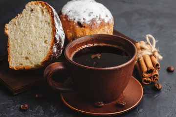 Cup with hot coffee, muffins and cinnamon sticks on the dark, textured background