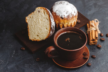 Cup with hot coffee, muffins and cinnamon sticks on the dark, textured background