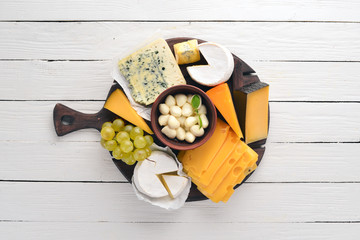 A large set of cheeses. Mozzarella, blue cheese, brie cheese, maasdam. Top view. On a white wooden...