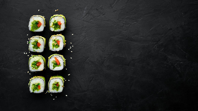 Sushi roll with avocado, cucumber and tomato. Japanese cuisine. Top view. On a black background.