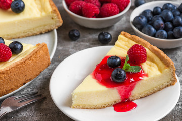 cheesecake with slice of cake with fresh raspberries, blueberries, jam and mint on concrete background. close up