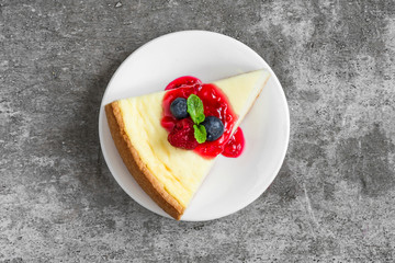 slice of cheesecake with fresh raspberries, blueberries, jam and mint on concrete background. top...