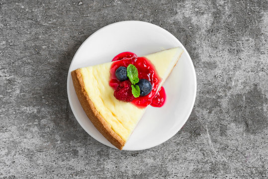 Slice Of Cheesecake With Fresh Raspberries, Blueberries, Jam And Mint On Concrete Background. Top View