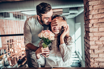 Surprise for you! Beautiful romantic couple in cafe. Young man is presenting flowers to his wife.