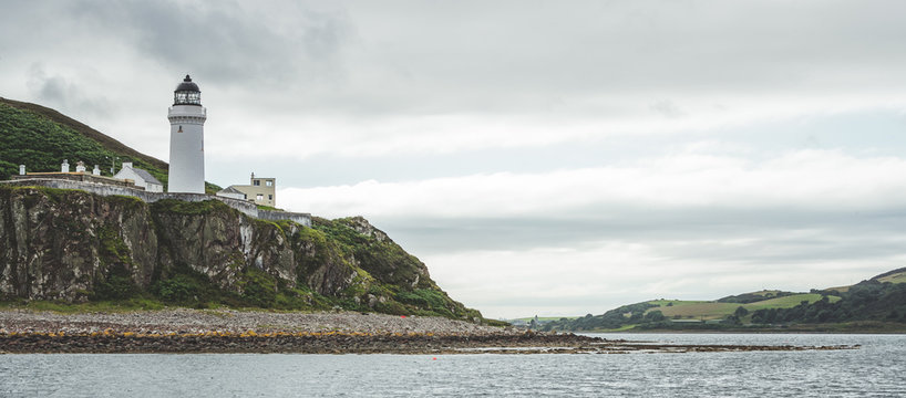 Irish shoreline panorama with Campbeltown lighthouse. Northern Ireland. Stunning English landscape. White lighthouse on the steep cliff. The shore panoramic view under the rainy cloudy sky.
