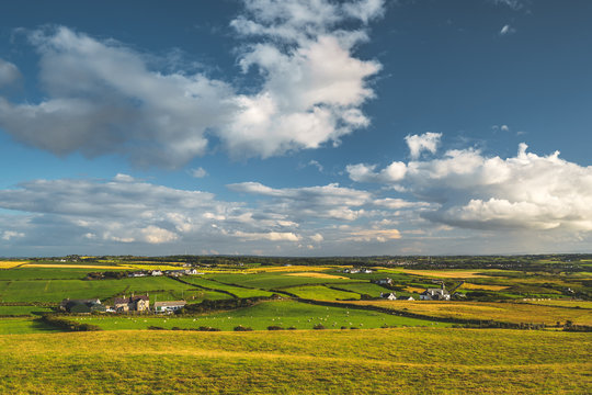 Irish countryside panoramic view. Green fields on the blue cloudy sky background. The farm cottages among the peaceful natural environment. Grass covered meadows on the sunset. Amazing horizon view.