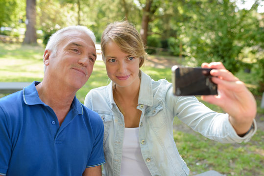 father and adult daughter taking a selfie outdoors