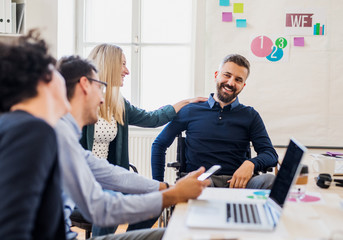 Young businessman in wheelchair with colleagues in a modern office.