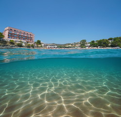 Spain beach with an hotel in Llanca on the Costa Brava and a sandy seabed underwater, split view half over and under water, Mediterranean sea, Platja de Grifeu, Catalonia