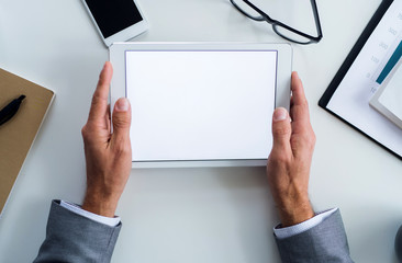 A midsection of businessman sitting at the table, using tablet. A top view. Copy space.