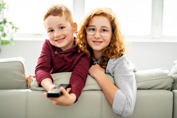 Happy girl and boy watching tv with remote control