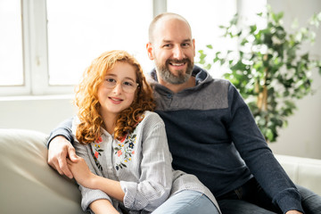 cheerful redhead father and daughter smiling at camera on sofa