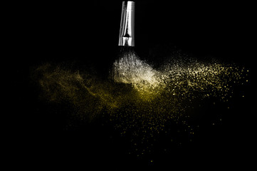 Cosmetic brush with golden cosmetic powder spreading for makeup artist and graphic design in black background