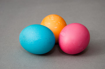 Three easter eggs blue pink orange color on a gray background. View from the side.