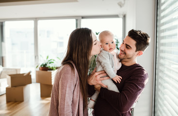 A portrait of young couple with a baby and cardboard boxes moving in a new home.
